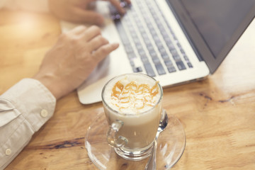 man's hand working with laptop computer with cup of hot latte co