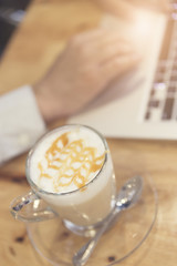 man's hand working with laptop computer with cup of hot latte co