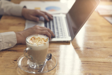 man's hand working with laptop computer with cup of hot latte co