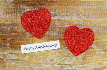 Happy Anniversary card with two sparkling red hearts on rustic wooden surface
