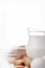 Glass jug with milk, wheat seeds and two eggs