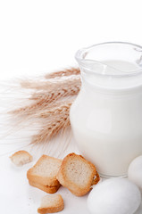 Glass jug with milk, wheat seeds and two eggs