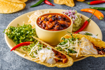 Tacos with chili con carne, salad, cheese and sour cream.