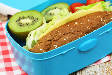 Healthy lunch consisting of brown cheese and lettuce roll, cherry tomatoes and kiwi fruit, closeup
