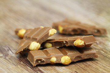 Pieces of milk chocolate with whole hazelnuts on rustic wooden surface
