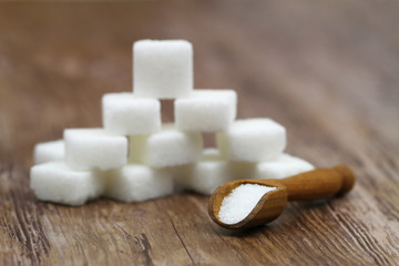 White sugar on wooden scoop and white sugar cubes stacked up in the background
