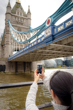 Woman taking pictures of the Tower Bridge with her phone, in London, England, UK