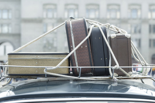 Vintage suitcases on the roof of the trunk of a car.