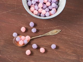 Round purple and pink candies in a bowl on wooden background, copy space