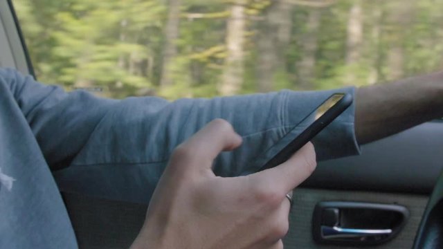 Young adult man swipes through his phone while driving a car 