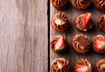 Chocolate cupcakes with strawberry and chocolate on a woodenrustic table. Top view.