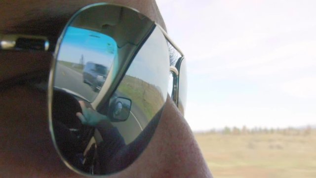 Close up shot of mans sunglasses showing the reflection of the road 