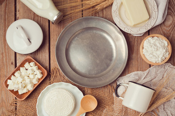Milk, cheese and butter around empty vintage plate on wooden table. Healthy eating concept. View from above. Flat lay.