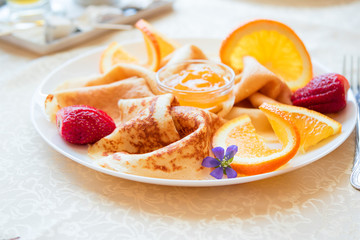 Closeup plate with pancakes with pieces of oranges, strawberries, jam and lavender flower