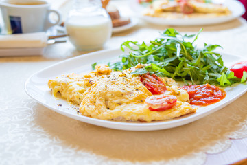 Omelet with cherry tomatos, arugula, ground pepper and sauce on white plate