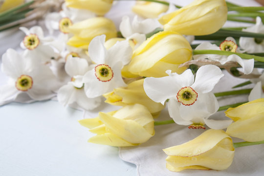 White daffodils narcissus and yellow tulips on a light wooden table. Beautiful spring floral background.