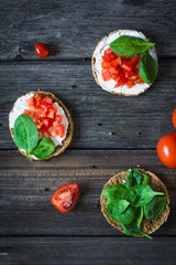 Healthy light snack toast with white cheese, tomato and baby spinach on rustic wooden backdrop. Top view, vertical composition