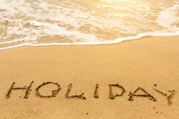 Fototapeta na wymiar Holiday - written on sandy beach with the soft wave.