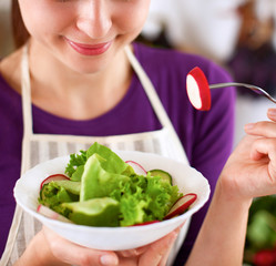 Young woman eating fresh salad in modern kitchen