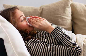 Portrait of a sick woman blowing her nose while sitting on the sofa 