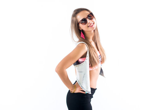 Young female model standing sideways, bending her body, putting arm on hip, wearing sunglasses and bright accessories.