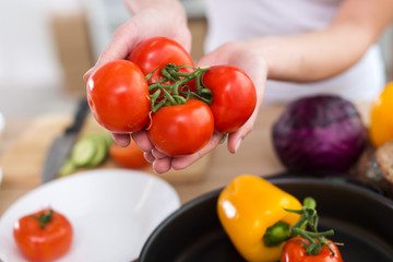 Close-up top view picture of female hands showing fresh juicy red tomatoes over the kitchen table, ready for cooking at home.
