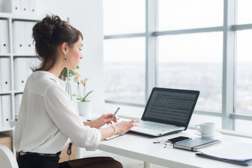 Rear view portrait of a businesswoman sitting on her workplace in the office, typing, looking at pc...