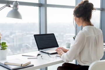 Woman wearing office suit sitting at her workplace, typing, searching new ideas for project. Female...