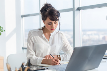 Female writer working in light modern office, writing down new ideas her notebook, searching...
