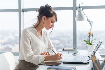 Young woman working as an office manager, planning work tasks, writing down her schedule to planner...