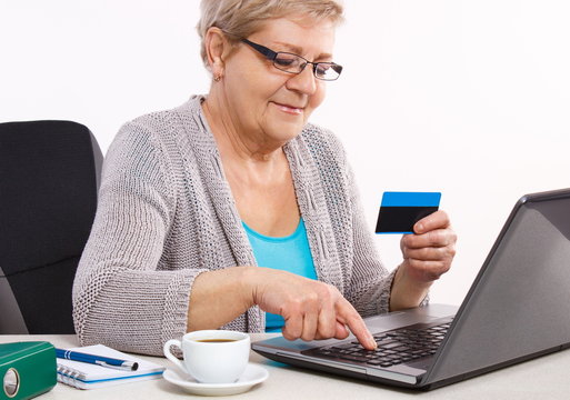 Elderly Senior Woman With Credit Card And Laptop Paying Over Internet For Utility Bills Or Online Shopping