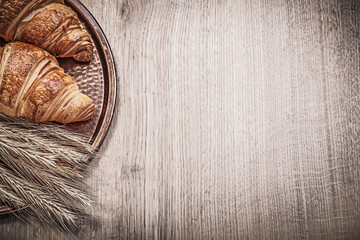 Golden wheat rye ears fresh-baked croissants copper tray on wood