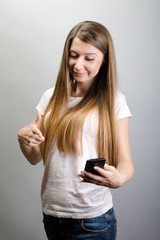 Portrait of an attractive happy brunette young woman pointing to her smart mobile phone, on grey background