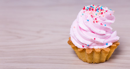 cup cake with pink cream over wooden background