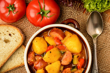 Vegetables stewed with pork sausages in ceramic pot.