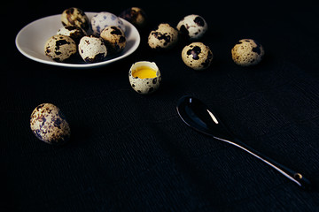 Quail eggs on a black textured background. Raw broken egg with the yolk. Easter card. Side view....