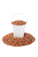 White bucket full of buckwheat, stands on a heap buckwheat
