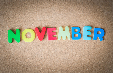 Colorful wooden word NOVEMBER on cork board with selective focus