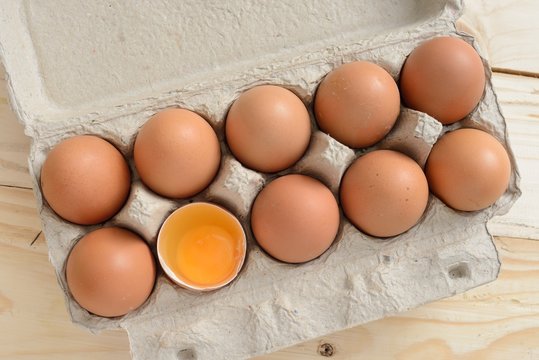 brown eggs in carton with broken egg