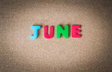 Colorful wooden word JUNE on cork board with selective focus