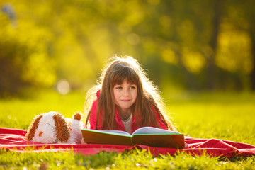 little girl lying on green grass in Park and reading a book. child plays outdoor