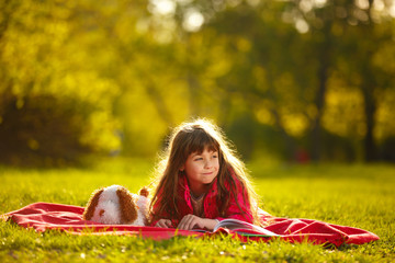 little girl lying on green grass in Park and reading a book. child plays outdoor