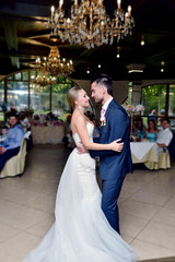 Wedding couple in the restaurant is dancing. Beautiful model girl in white dress. Handsome man in suit. Beauty bride with groom. Female and male portrait. Woman with lace veil. Lady and guy indoors