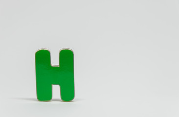 Fototapeta premium Green wooden alphabet H with white background and selective focus