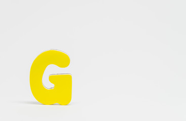 Yellow wooden alphabet G with white background and selective focus