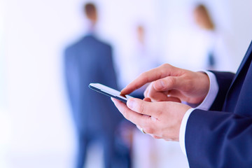 Portrait of young businessman in office with colleagues in the background and using mobile