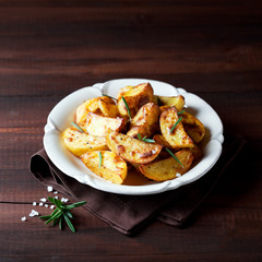 Roasted potato wedges with rosemary on plate, selective focus
