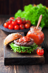 Fresh homemade burger on wooden cutting board with spicy tomato sauce, selective focus