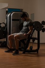 Fototapeta na wymiar Young Bodybuilder Exercising Biceps On Machine