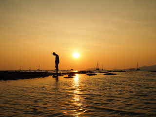 Silhouette of sad young man standing dejectedly turn back to the sun at sea beach with beautiful sky sunset background.